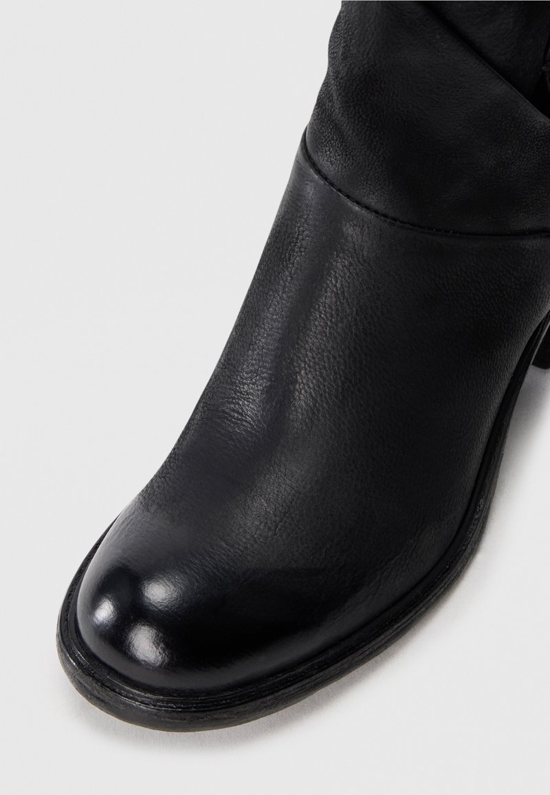 Gros plan sur une botte de cheville en cuir noir avec un bout arrondi et un petit talon sur fond blanc.