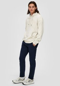 Crème hoodie met kangoeroezak en verstelbare trekkoorden, gecombineerd met marineblauwe broek en lichtgekleurde sneakers; minimalistisch ontwerp.