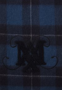 Blå og sort plaid uldstof med en blød tekstur. Har et fremtrædende sort broderet logo med kurver og "Co." under.