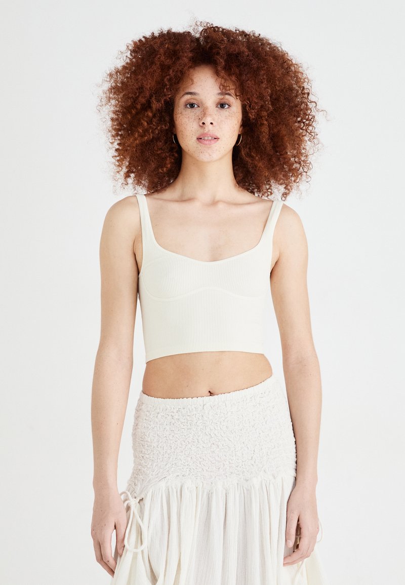 Ribbed cream bralette with wide straps and a square neckline, paired with a textured off-white skirt featuring an elastic waistband.