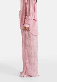 Lange roze plissés rok met een vloeiende vormgeving, voorzien van gestructureerde verticale lijnen en zijsplitten aan de zoom voor extra beweging.