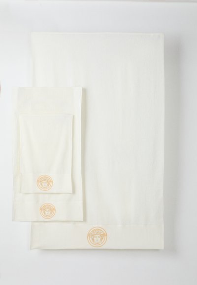 Set de trei prosoape albe de dimensiuni diferite, cu o țesătură texturată și logo brodat portocaliu la tivul fiecărui prosop.