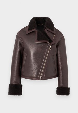 Smeđa kožna skraćena jakna s krznom od umjetne kože, zatvaranjem na cipzar i rukavima od ovčjeg krzna. Ima asimetričan dizajn i teksturiranu završnu obradu.