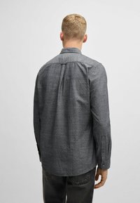 Camisa gris de botones con tela texturizada, patrón sutil y mangas largas. Presenta un cuello y puños abotonados. Se muestra vista trasera.