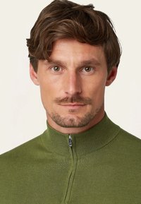 Groene ritspullover met hoge kraag, gemaakt van geribde tricotstof. Beschikt over een voorkant met rits en een subtiel patroon.