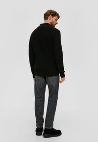 Zwarte gebreide trui met een kraag, gedragen met donkergrijze spijkerbroek en zwarte schoenen, gezien vanaf de achterkant. Zachte textuur en casual pasvorm.