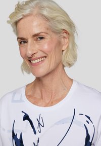 Weißes T-Shirt mit abstrakten blauen Mustern und Designelementen. Weicher Stoff, runder Halsauschnitt und kurze Ärmel.