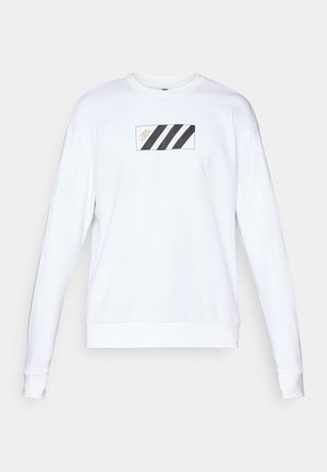 Biela mikina s rímskym nášivom, na ktorom sú tri čierne diagonálne pruhy a zlatý nápis. Mäkká látka, dlhé rukávy a rebrované manžety.