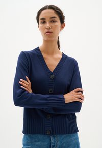 Marinblå kavaj med V-ringning, ribbade ärmslut och fem knäppningar. Har en figursydd midja och mjuk textur för komfort.
