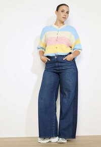 Kleurige gestreepte cardigan in pastelkleuren, zachte textuur, gecombineerd met hoge taille wijde denim jeans in diepblauw. Witte sneakers maken de look af.