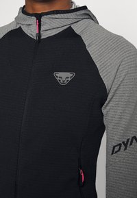 Giacca con cappuccio caratterizzata da un corpo nero e dettagli grigi. Maniche grigie strutturate, chiusura con zip e cursore della zip rosa. Logo sul petto.