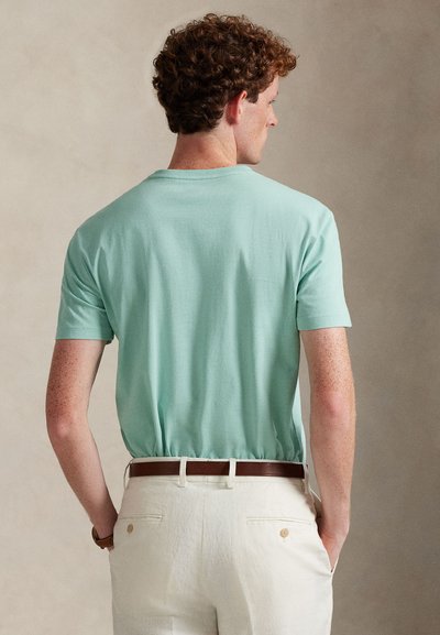 Μέντα πράσινη κοντομάνικη μπλούζα με στρογγυλή λαιμόκοψη, κατασκευασμένη από μαλακό ύφασμα, συνδυασμένη με ανοιχτόχρωμο παντελόνι και καφέ ζώνη.