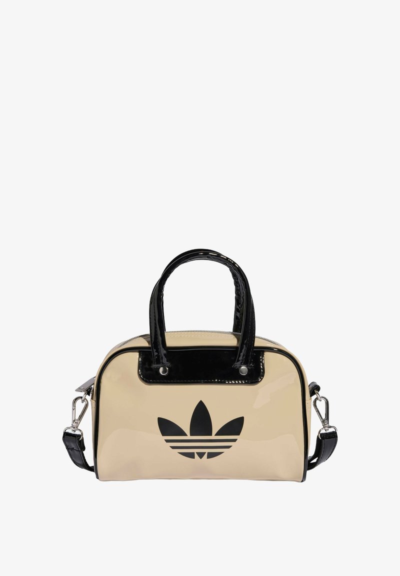 Beżowa torba z lakierowanej skóry z czarnymi akcentami, z dwoma uchwytami i odczepianym paskiem na ramię. Z przodu czarny wzór logo.