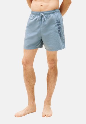 Pantalones de baño azul claro hechos de un material ligero, con una cinturilla elástica con cordón y un logo impreso en el costado.
