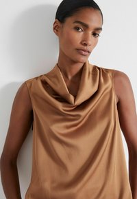 Brown draped sleeveless top made from smooth fabric, featuring a cowl neck design and a relaxed fit, showcasing soft folds and texture.