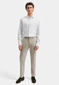 Vit långärmad skjorta med knappar, beige skräddarsydda byxor och mörkbruna skor. Slim fit, slät tygkvalitet och klassisk kragdetalj.