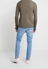 Maglione verde oliva a coste, jeans slim fit azzurri con orlo sfrangiato, sneakers bianche. Design minimalista con dettagli hardware di base.