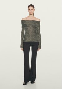 Top a spalle scoperte, in metallo nero, con maniche lunghe e lavorazione a maglia, abbinato a pantaloni neri aderenti a zampa e scarpe lucide nere.