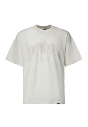 T-shirt bianca a maniche corte con collo rotondo e testo beige chiaro "OWNER CLUB" sul davanti e una piccola etichetta nera sull'orlo inferiore.