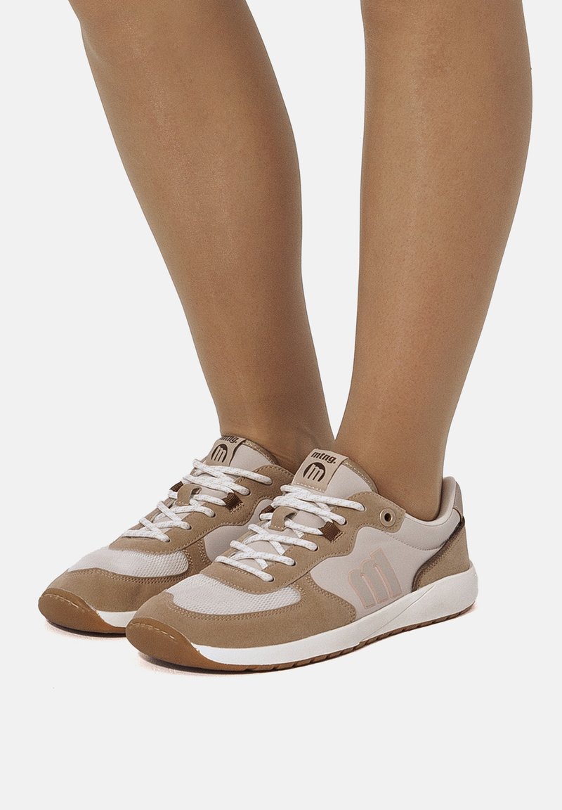 Beige Sneaker mit weißen und hellbraunen Akzenten. Merkmale sind ein Obermaterial aus Wildleder und Mesh, eine Schnürung und eine Gummisohle.