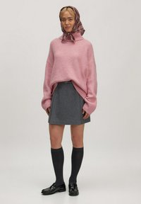 Roze gebreide trui met een losse pasvorm en hoge kraag, grijze wollen rok, donkere kniehoge sokken en zwarte instappers. Inclusief een geruit hoofddoek.