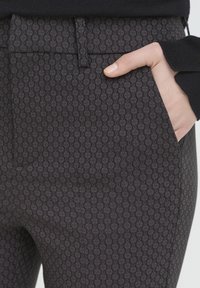 Dark patterned trousers featuring a subtle diamond design, with a flat waistband and side pockets, made from a smooth fabric.