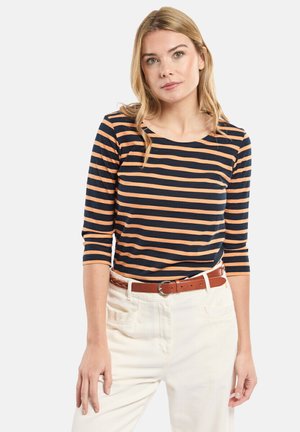 Haut à manches longues rayé bleu marine et orange avec un col rond, associé à un pantalon blanc et une ceinture marron, avec une coupe décontractée.