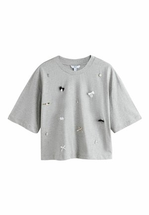 Světlé šedé krátké tričko s krátkým rukávem a oříznutým střihem, ozdobené malými dekorativními prvky včetně mašliček, klíče, květiny a hodinek rozmístěných na přední straně.