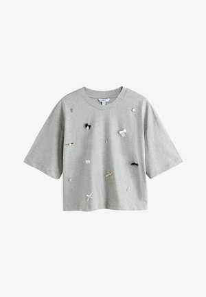 Jasnoszary krótki t-shirt z krótkim rękawem, przycięty, z małymi ozdobnymi elementami, takimi jak kokardki, klucz, kwiat i zegar rozmieszczone na przodzie.