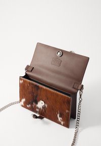 Brun læder- og teksturert pels crossbody taske med en sølv knaplukning, kædetras, og logo indeni, der har et blandet brun og hvid mønster.