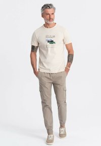 Beige katoenen T-shirt met abstracte grafische print in groen- en tinten blauw, gecombineerd met licht khaki cargobroek met zakken en elastische boorden.