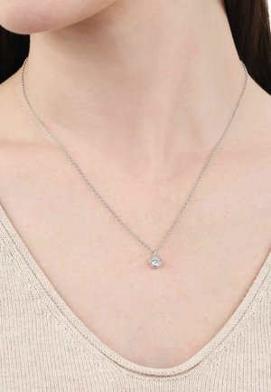 Collar de cadena de plata con colgante redondo de piedra preciosa transparente, llevado en el cuello de una persona sobre un top de punto beige.