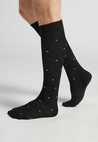 Svarta knästrumpor med en slät textur som har ljusgrå prickar över hela. Elastisk nederkant för en säker passform.