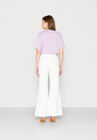 Camisa lilás de manga curta, corte descontraído; combinada com calças brancas de pernas largas; acessorizada com mules laranjas de salto. Fundo plano.