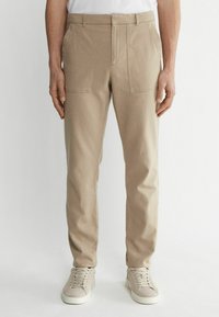 Beige Baumwollmischungshosen mit geradem Beindesign, ausgestattet mit Fronttaschen und Gürtelschlaufen. Getragen mit hellen Sneakers.