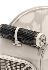 Covoraș din plasă neagră rulat, fixat cu o curea bej în interiorul unei genți din material textil bej, prevăzută cu fermoar și buzunar din plasă.