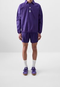 Lila idrottströja med krage, tillsammans med randiga lila shorts och lila basketskor med gummisula och vita strumpor.