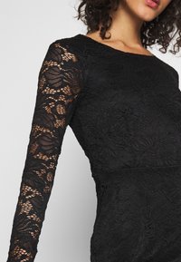 Svart spetsklänning med långa ärmar, blommönster, strukturerad yta och en figurnära silhuett, med rund halsringning.