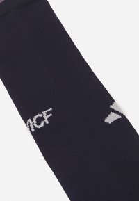 Calcetín deportivo de color navy hecho de tela texturizada con logo y acentos en blanco. Presenta un diseño acanalado en la parte superior y lateral.