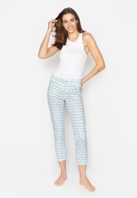 Witte, mouwloze tanktop gecombineerd met cropped pants met een lichtblauw, golfachtig patroon. Model staat blootvoets in een ontspannen houding.