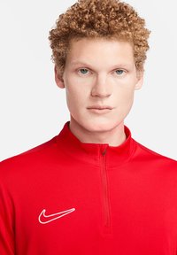 Rode Nike pullover met een hoge kraag en korte rits. Bevat een witte Nike-logo aan de linkerkant. Soepele textuur met een getailleerd ontwerp.