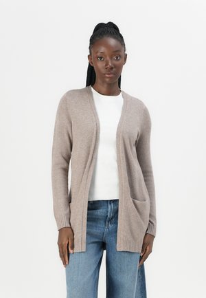 Lys brun cardigan med en avslappet passform, åpen front, ribbestrikkede mansjetter og to frontlommer, brukt over en hvit skjorte, sammen med denim jeans.