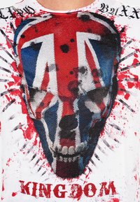 Witte T-shirt met een rood, blauw en zwart schedelontwerp met de Union Jack. De tekst "KINGDOM" staat in vet rood onderaan.