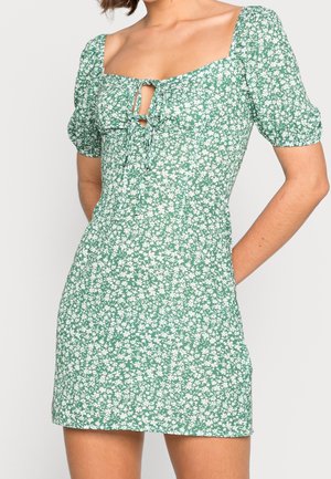 Groene bloemenjurk met een vierkante halslijn, pofmouwen en een strikdetail aan de voorkant. Gemaakt van lichtgewicht stof met een gestructureerd patroon.