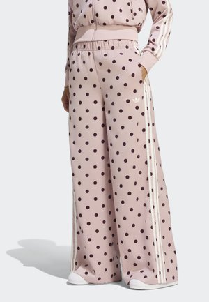 Personne portant un pantalon rose taille haute à jambes larges avec des pois noirs et des bandes blanches sur les côtés, associé à une veste assortie et des chaussures blanches.