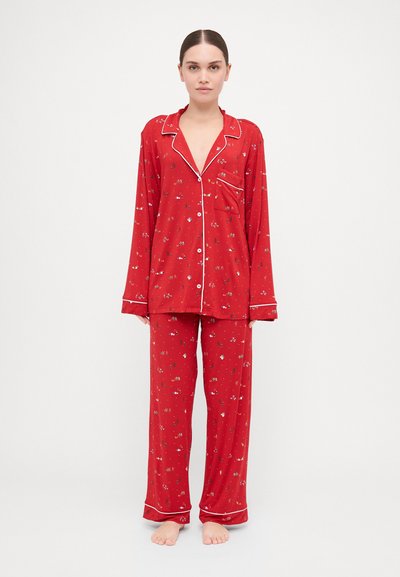 Red pajama set featuring long-sleeve top and matching pants. Material is soft with a floral pattern, accented by white piping along edges.