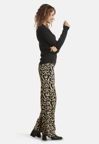Black long-sleeve sweater paired with patterned flared trousers in black and cream. Model wears block-heeled ankle boots. Curly hair styled down.