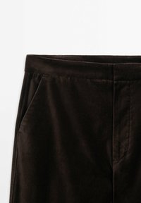 Pantalon en velours noir avec une taille ajustée et des poches latérales, présenté sur un fond blanc uni.