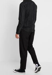 Zwarte denim shirt met lange mouwen, gebogen zoom en knoopsluiting, gecombineerd met zwarte broek en zwarte hoge sneakers.