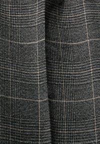 Černá a šedá kostkovaná látka s texturovanou vazbou. Vzor obsahuje tenké čáry, které vytvářejí mřížkový design po celém povrchu.